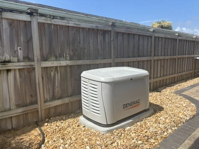 Generac home standby generator installed on a concrete pad beside a wooden privacy fence