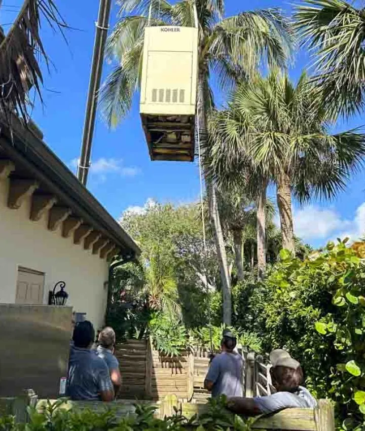 Crane lifting a Kohler home generator into place for a residential installation